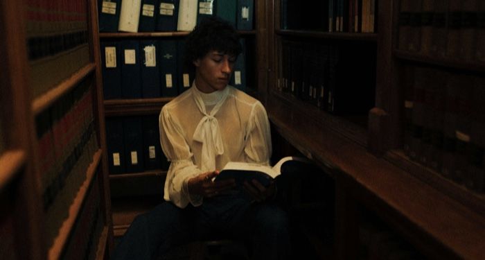 a lighter skinned masc presenting person reading a book in a dark corner of a library.jpg.optimal