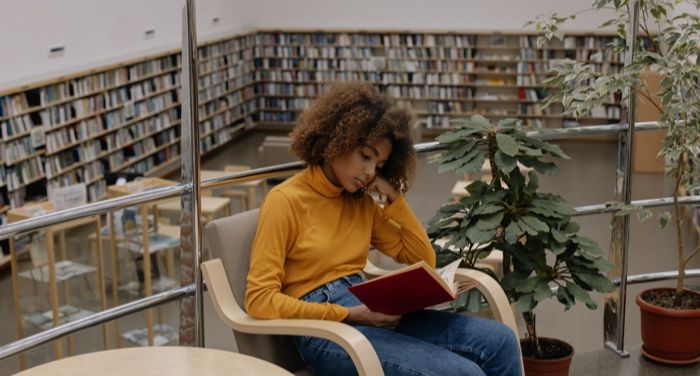 tan skinned young Black woman or teen reading in a library.jpg.optimal