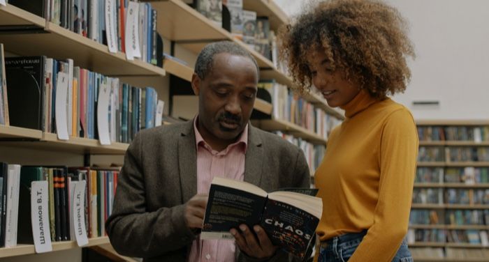 a Black man and young woman discussing a book in a library.jpg.optimal