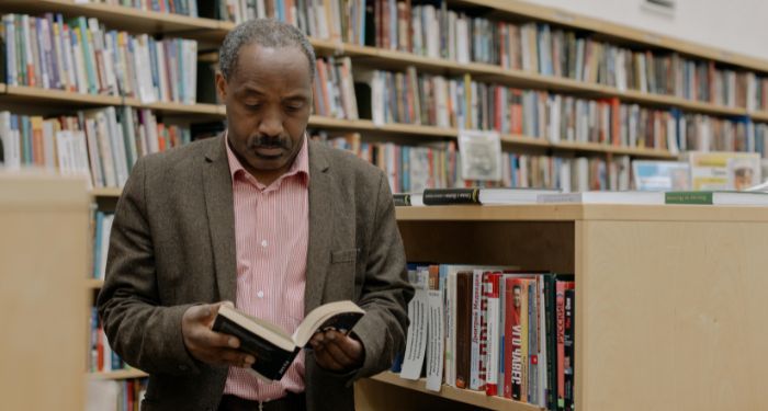 older brown skinned Black man reading in a library.jpg.optimal