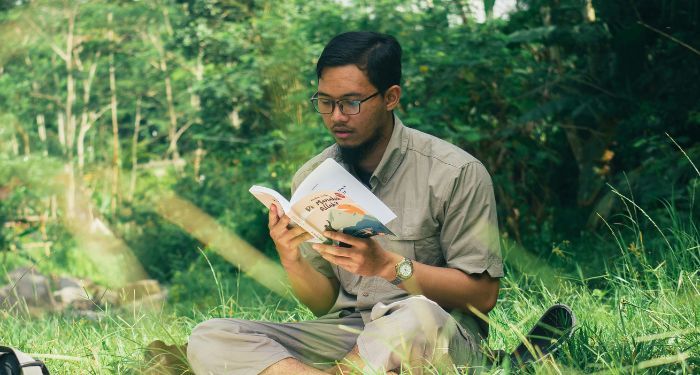 Asian man reading a book on grass.jpg.optimal