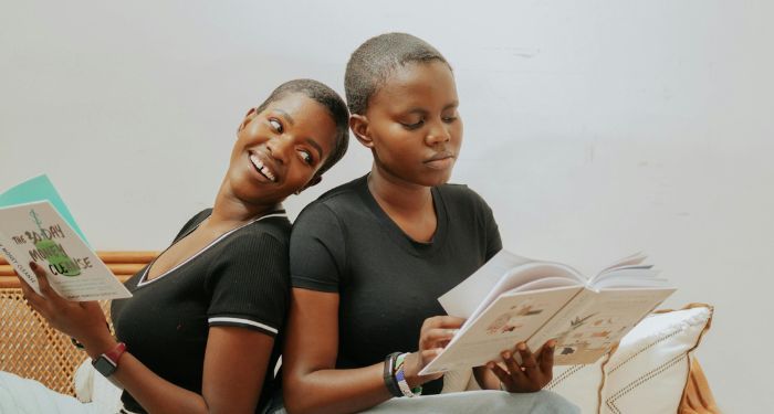 two brown skinned Black women with short haair sitting back to back and reading books.jpg.optimal